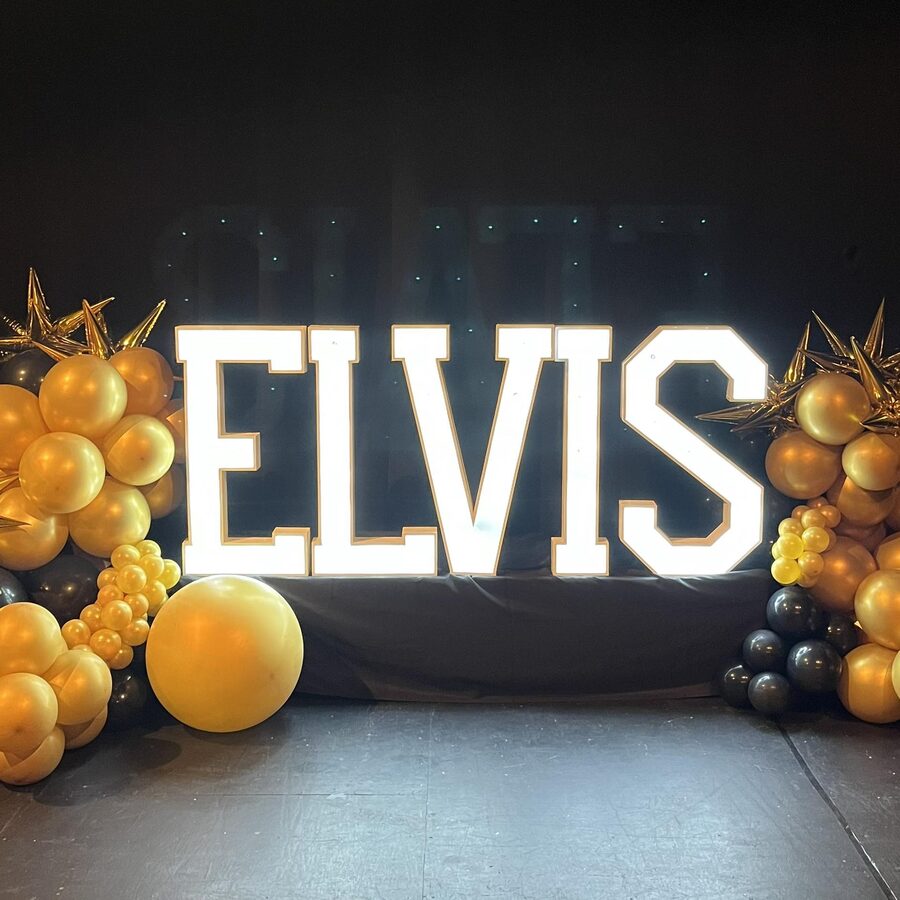 ELVIS in lit letters surrounded by gold balloons and stars