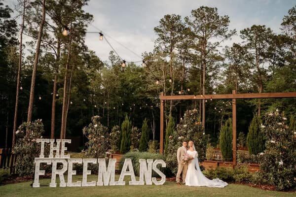 THE FREEMANS in lit letters on a lawn behind a bride and groom