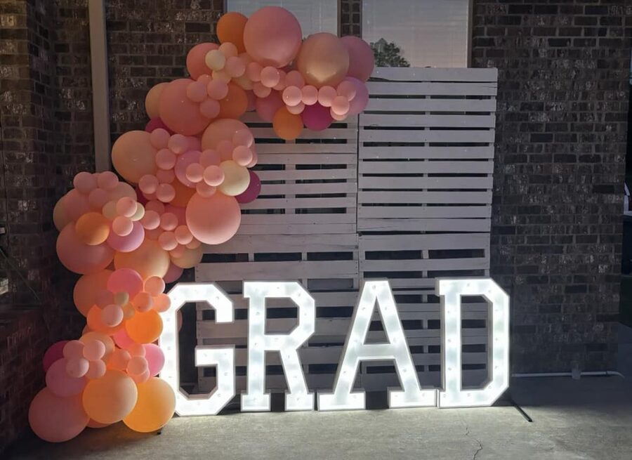 GRAD in lit letters beside a blush balloon garland