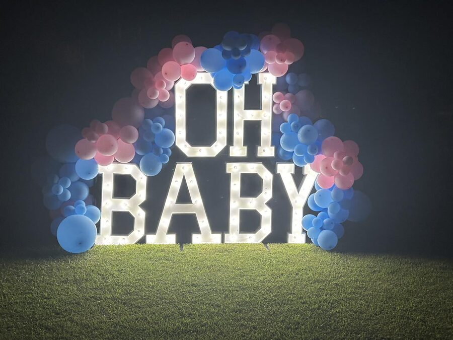 OH BABY in lit letters framed by a pink and blue balloon arch